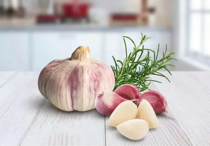 Knoblauchzehen und ein Rosmarinzweig auf einem Holztisch. Vorsicht bei der Zubereitung von Knoblauchöl, um Botulismus zu vermeiden.