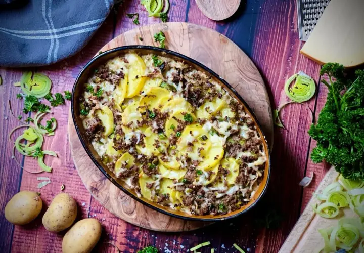 Herzhafter kartoffelauflauf aus rohen Kartoffeln mit Hackfleisch, überbacken mit Käse. Garniert mit Petersilie und Lauch.