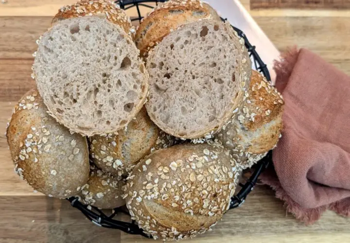 Korb mit knusprigen Haferbrot-Brötchen, eines davon aufgeschnitten, zeigt die luftige Krume.