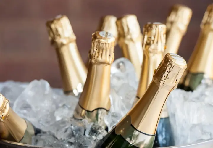 Mehrere Champagnerflaschen in goldenen Kapseln kühlen in einem Eisbad. Die perfekte Champagner Temperatur für den Genuss.