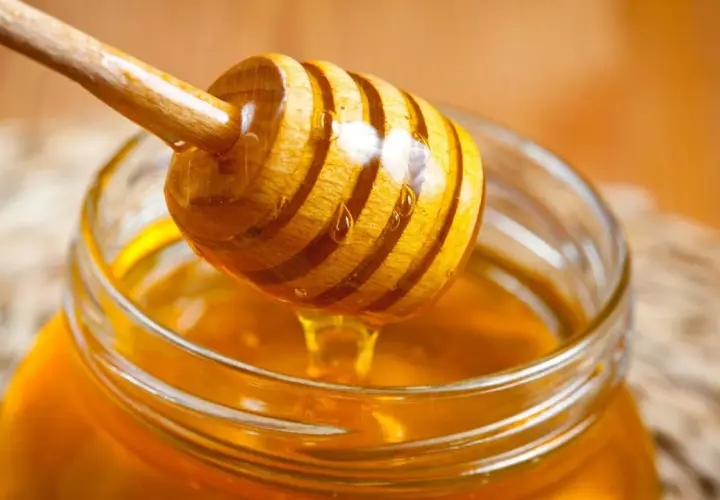 Ein Honigheber aus Holz tropft goldenen Honig in ein Glas. Kein Anzeichen von honig schimmel.