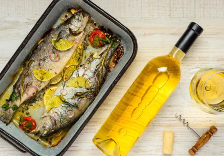 Zwei gebackene Forellen mit Zitrone und Kräutern, daneben eine Flasche Weißwein und ein Glas. Perfekt, welcher Wein zu Lachs passt, ist hier schon fast klar.
