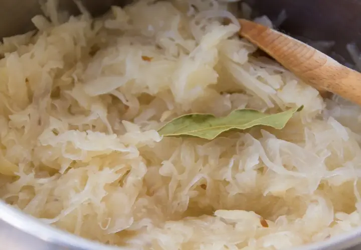 Frisch zubereitetes Sauerkraut mit Lorbeerblatt und einem Holzlöffel. Perfekt als Beilage zu einem herzhaften Gericht, vielleicht mit einem Glas Wein.