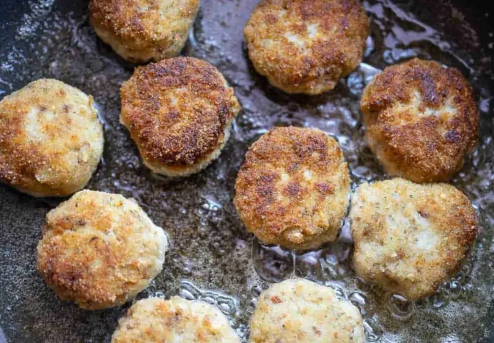 Mehrere goldbraune hackfleisch frikadellen brutzeln in heißem Öl in einer Pfanne.