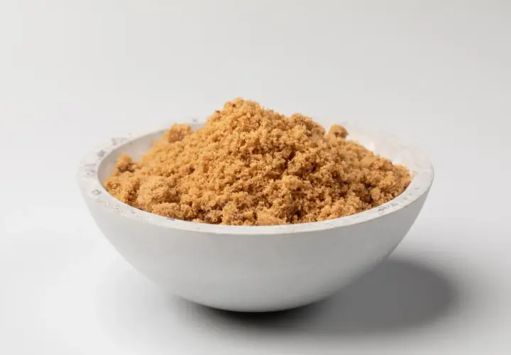 Schüssel mit dunklem Muscovado-Zucker, dessen feine Körner eine warme, karamellige Farbe haben.