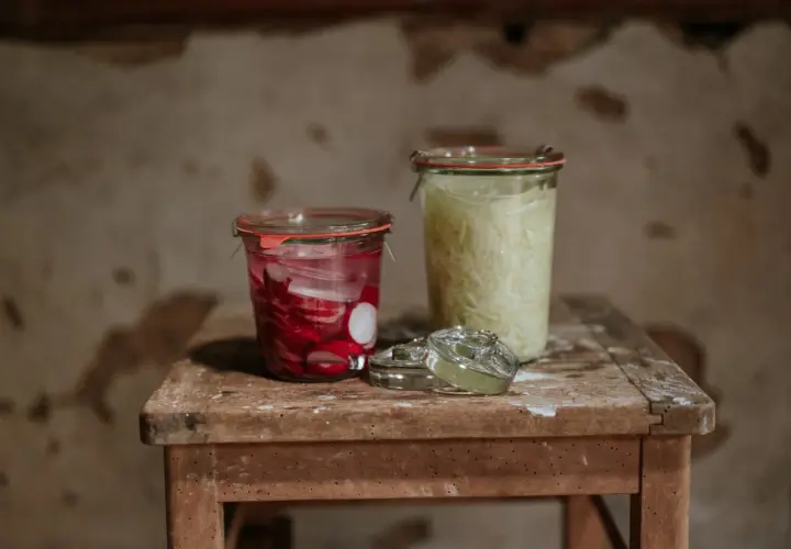Zwei Gläser mit fermentierten Lebensmitteln: links eingelegte Radieschen, rechts fermentiertes Sauerkraut.