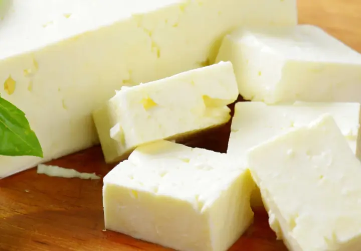 Frischer Feta, leicht schleimig, liegt auf einem Holzbrett, daneben grüne Basilikumblätter.