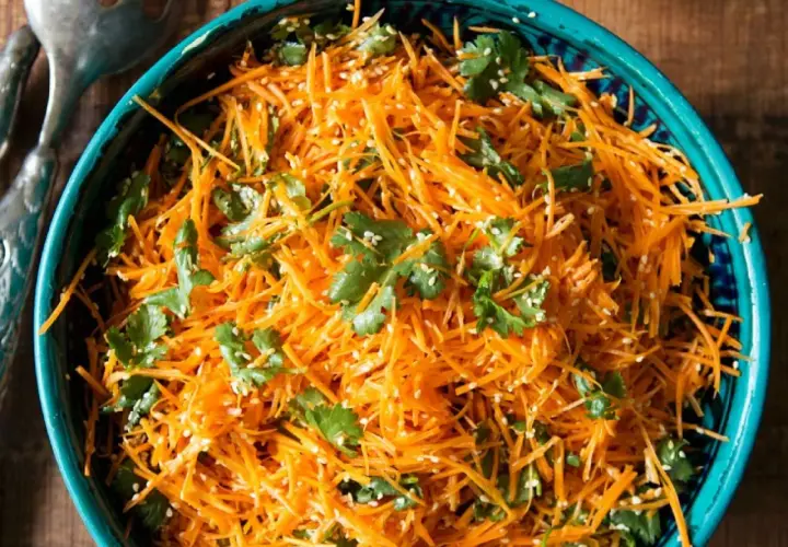 Ein erfrischender eiskraut salat aus geraspelten Karotten, garniert mit Koriander und Sesam.