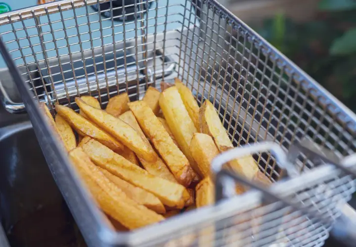 Goldgelbe Pommes in einem Frittierkorb, bereit, um sie wieder knusprig zu machen.