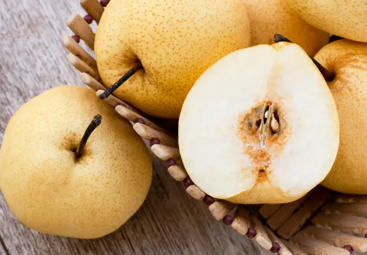 Nashi Birnen, deren Herkunft in Asien liegt, in einem Korb. Eine Frucht ist halbiert und zeigt das saftige Innere.