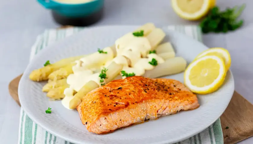 Gebratener Lachs mit weißem Spargel und cremiger Hollandaise. Ein klassisches Rezept mit Holllandaise, garniert mit Petersilie und Zitronenscheiben.