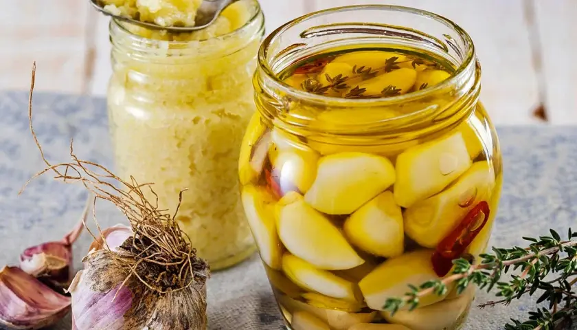 Eingelegter Knoblauch in Öl, daneben ein Glas mit Knoblauchpaste. So legt man Knoblauch ein für mehr Aroma.