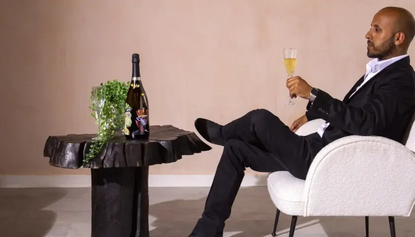 Ein Mann in schwarzem Anzug genießt ein Glas Champagner neben einer Flasche, die wie der teuerste Champagner der Welt aussieht.