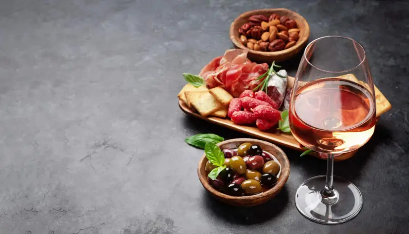 Ein Glas Roséwein als Aperitif, dazu eine Auswahl an Aufschnitt, Oliven und Nüssen. Perfekt für einen entspannten Abend.