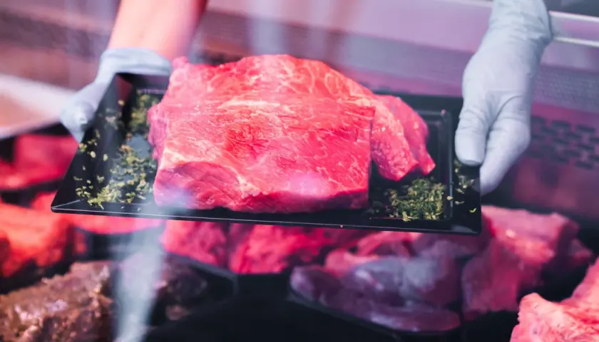 Frisch präsentiertes Rindfleisch auf einem schwarzen Teller, umgeben von Kräutern. Hoffentlich riecht das Rindfleisch nicht sauer.