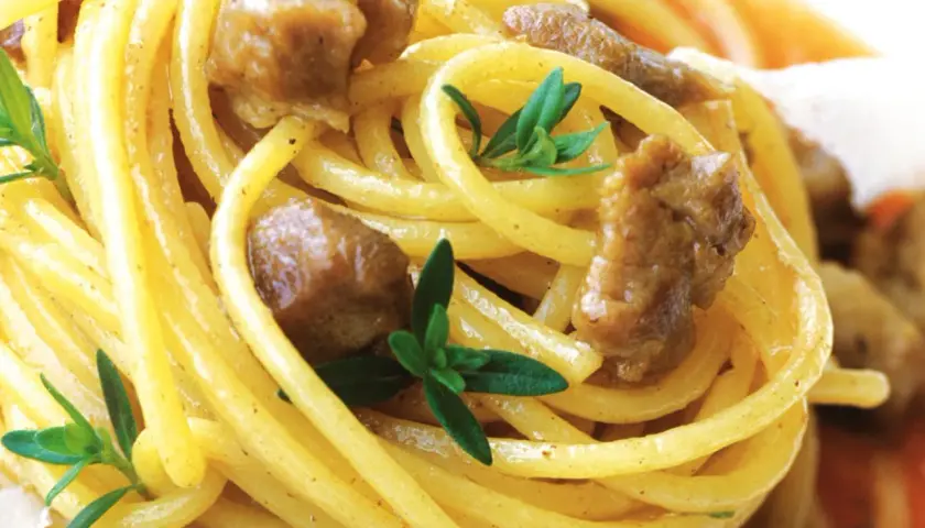 Spaghetti alla chitarra mit Fleischstücken und frischen Kräutern, ein köstliches Gericht.