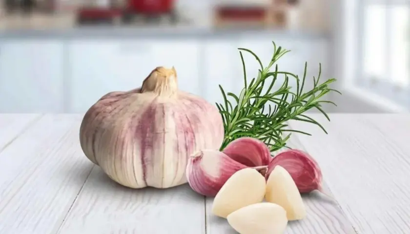 Knoblauchzehen und ein Rosmarinzweig auf einem Holztisch. Vorsicht bei der Zubereitung von Knoblauchöl, um Botulismus zu vermeiden.