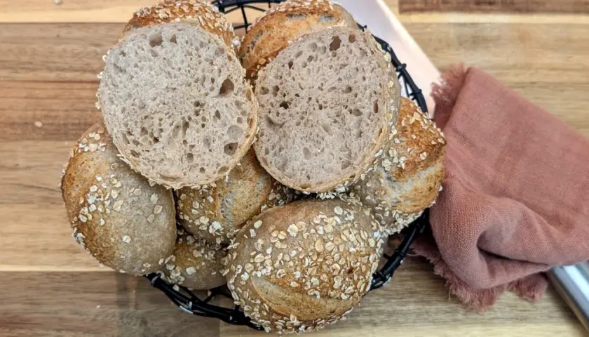 Korb mit knusprigen Haferbrot-Brötchen, eines davon aufgeschnitten, zeigt die luftige Krume.