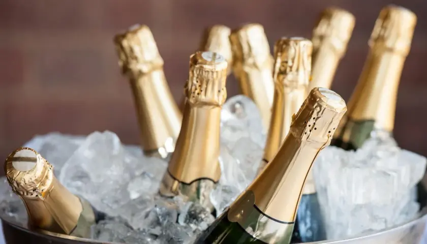 Mehrere Champagnerflaschen in goldenen Kapseln kühlen in einem Eisbad. Die perfekte Champagner Temperatur für den Genuss.