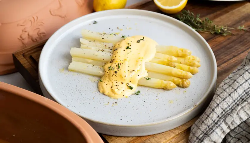 Frischer weißer Spargel aus dem Glas, verfeinert mit cremiger Sauce Hollandaise und Kräutern, garniert mit Pfeffer und Zitronenschale.
