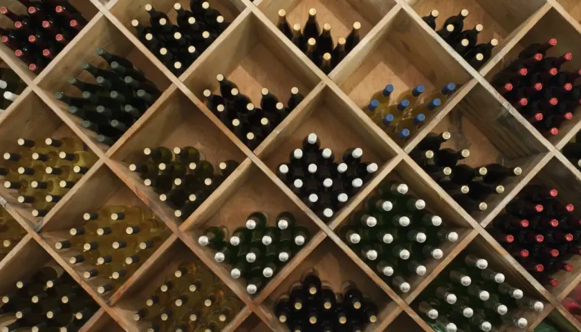 Weinregal mit vielen Flaschen Rotwein und Weißwein. Die Frage, wie lange kann man Rotwein lagern, wird hier durch die Vielfalt der Flaschen angedeutet.