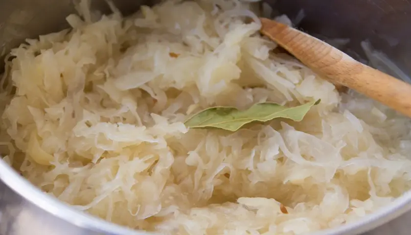 Frisch zubereitetes Sauerkraut mit Lorbeerblatt und einem Holzlöffel. Perfekt als Beilage zu einem herzhaften Gericht, vielleicht mit einem Glas Wein.