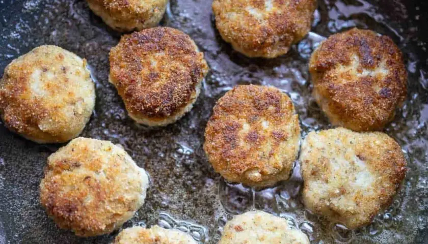 Mehrere goldbraune hackfleisch frikadellen brutzeln in heißem Öl in einer Pfanne.