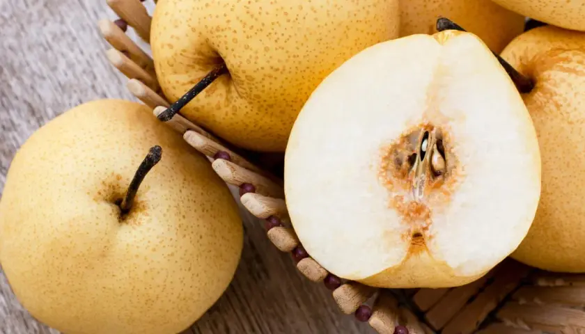 Nashi Birnen, deren Herkunft in Asien liegt, in einem Korb. Eine Frucht ist halbiert und zeigt das saftige Innere.