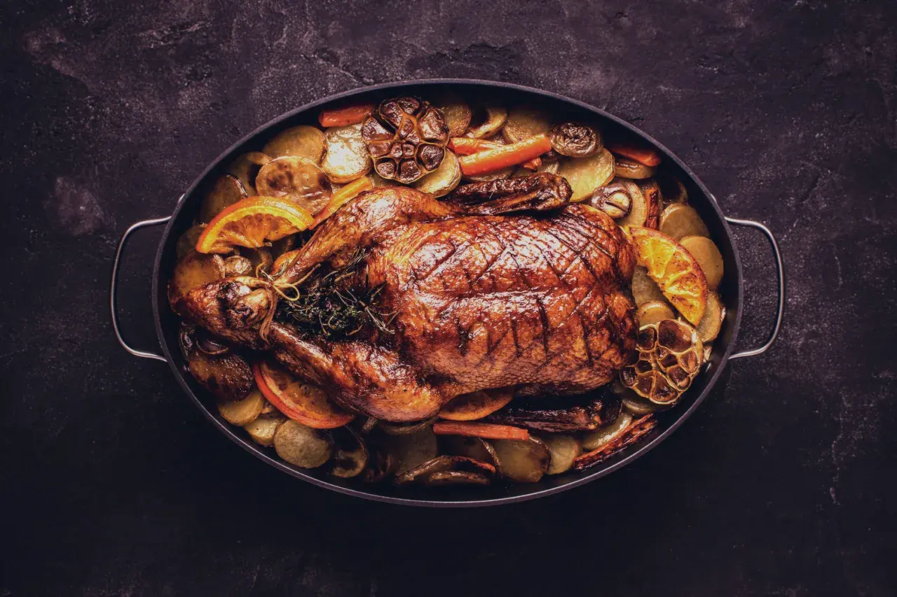 Ein goldbraun gebratener Gänsebraten mit Kartoffeln, Karotten und Orangenscheiben. Perfekt für die Frage: welcher Wein zu Gans?