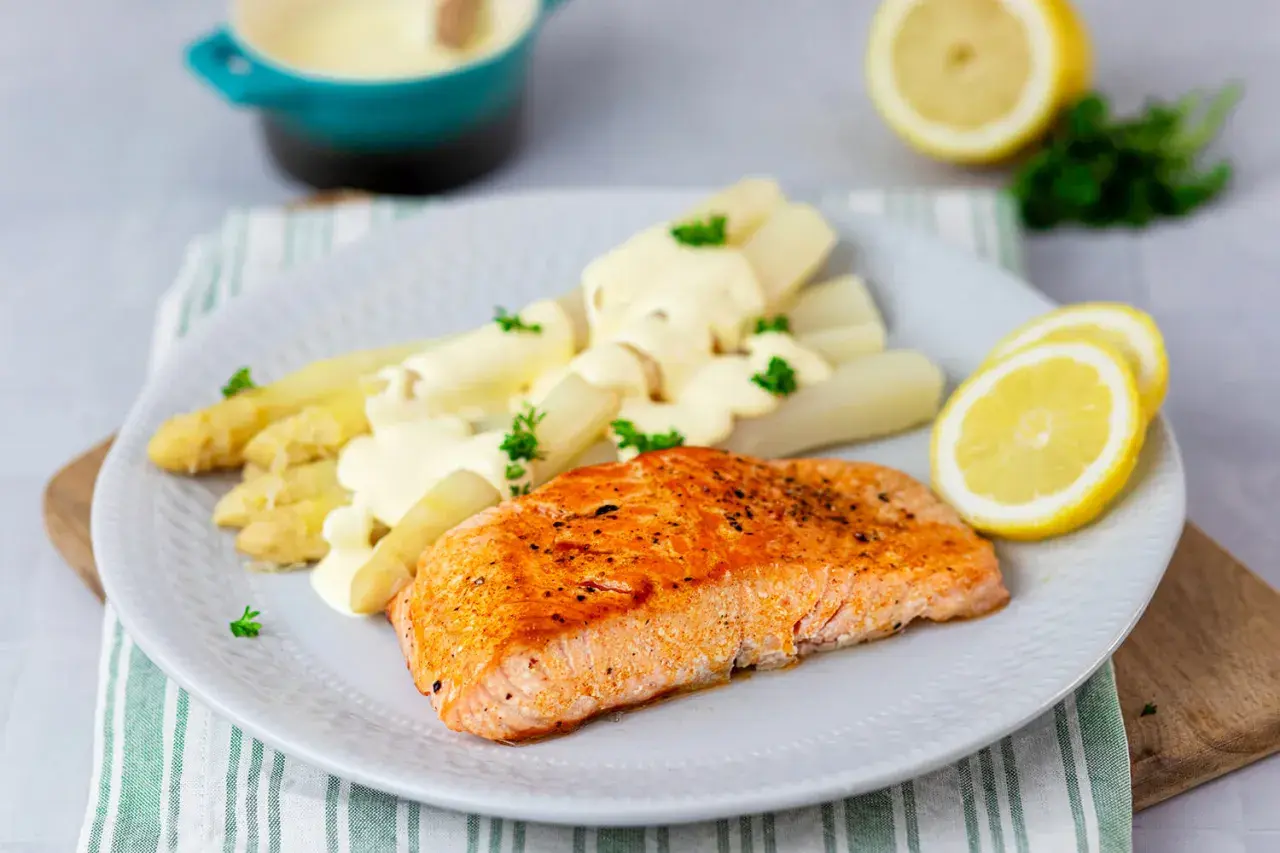 Gebratener Lachs mit weißem Spargel und cremiger Hollandaise. Ein klassisches Rezept mit Holllandaise, garniert mit Petersilie und Zitronenscheiben.
