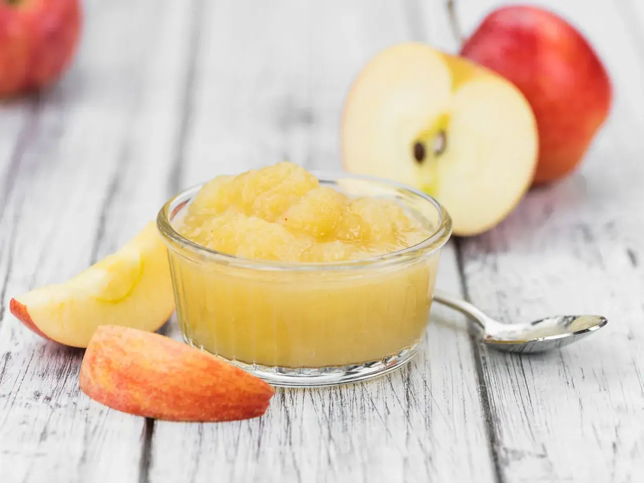 Apfelmus in einer Schale, umgeben von Apfelstücken und ganzen Äpfeln. Perfekt für leckere Rezepte mit Apfelsaft.