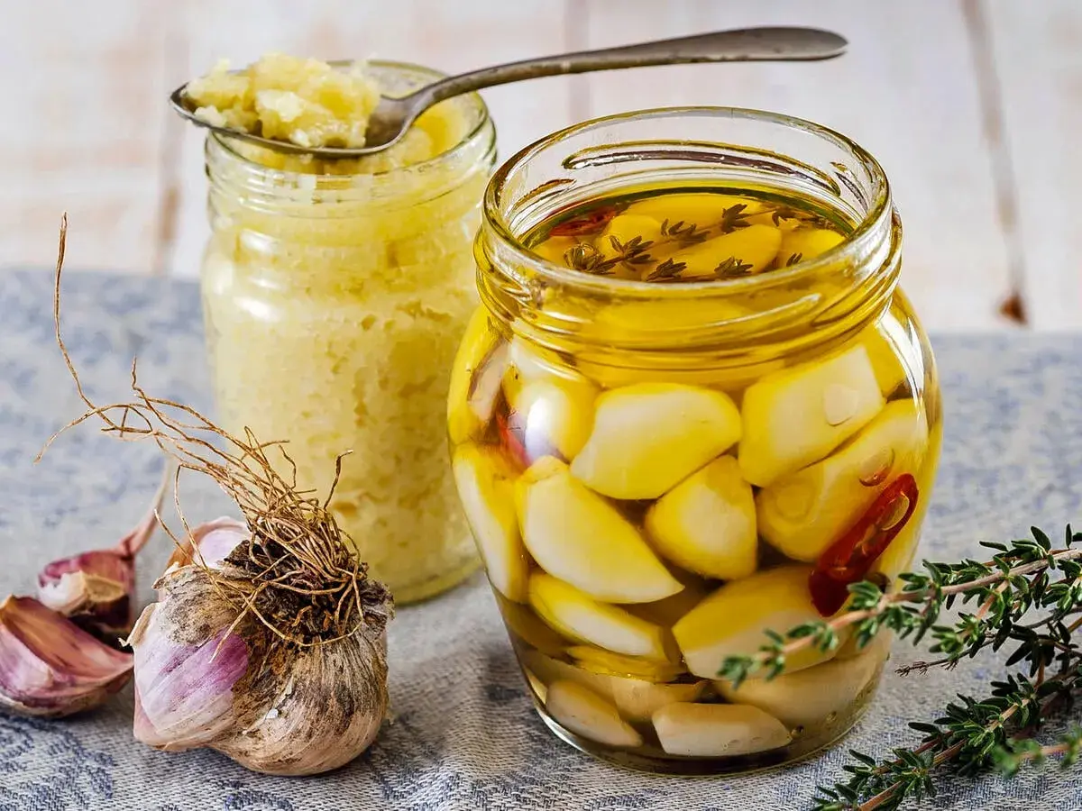 Eingelegter Knoblauch in Öl, daneben ein Glas mit Knoblauchpaste. So legt man Knoblauch ein für mehr Aroma.