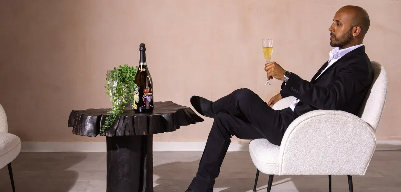 Ein Mann in schwarzem Anzug genießt ein Glas Champagner neben einer Flasche, die wie der teuerste Champagner der Welt aussieht.