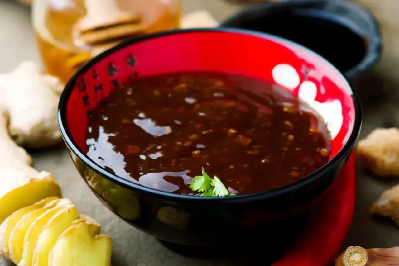 Schwarze Schüssel mit glänzender, dunkler Teriyaki-Sauce, umgeben von frischem Ingwer und Chili.