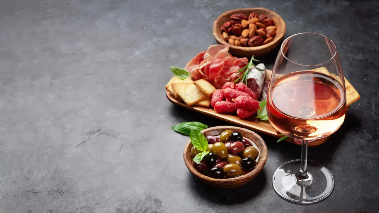 Ein Glas Roséwein als Aperitif, dazu eine Auswahl an Aufschnitt, Oliven und Nüssen. Perfekt für einen entspannten Abend.