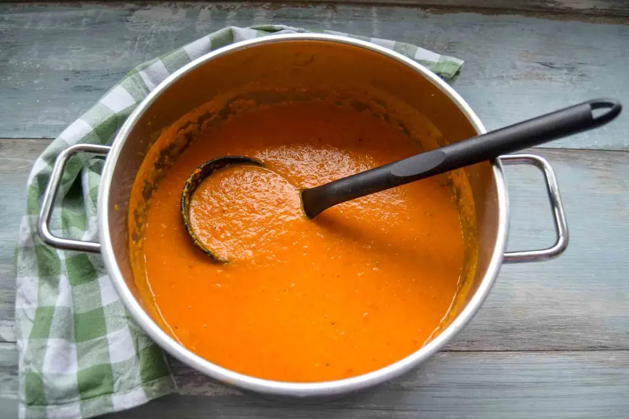 Ein Topf mit cremiger roter Linsensuppe mit Kokosmilch, bereit zum Servieren. Ein grünes Karotuch liegt daneben.