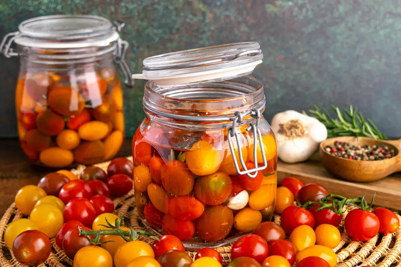 Gläser mit bunten Kirschtomaten, bereit zum **Tomaten fermentieren**. Daneben Knoblauch, Rosmarin und Pfefferkörner.