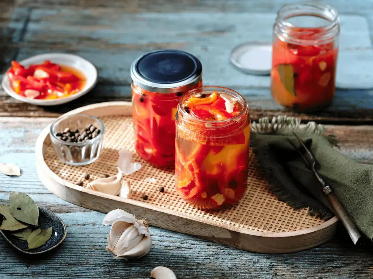 Zwei Gläser mit eingelegten Paprikastreifen, Knoblauch, Pfefferkörnern und Lorbeerblättern. Der Prozess des Paprika fermentieren ist hier gut sichtbar.