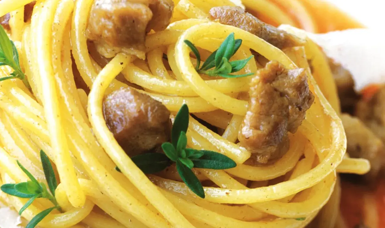 Spaghetti alla chitarra mit Fleischstücken und frischen Kräutern, ein köstliches Gericht.