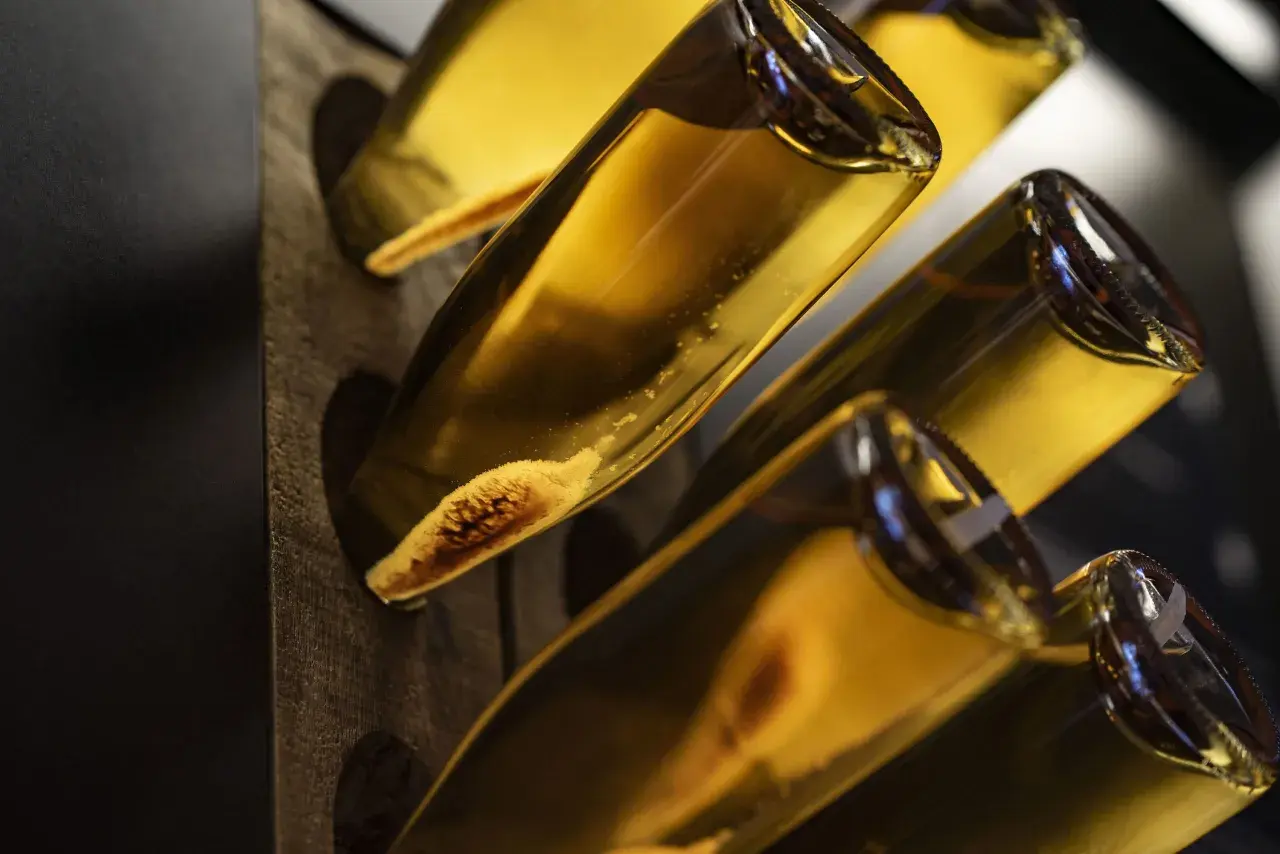 Flaschen mit goldgelbem Inhalt, vielleicht ein cremiger Wein oder ein süßer Likör. Die Sedimente am Flaschenboden deuten auf eine traditionelle Herstellung hin.