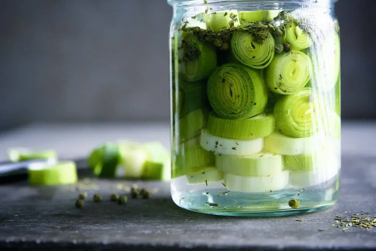 Ein Glas mit geschnittenem Lauch, bereit zum lauch fermentieren. Grüne Pfefferkörner und Kräuter sind ebenfalls zu sehen.