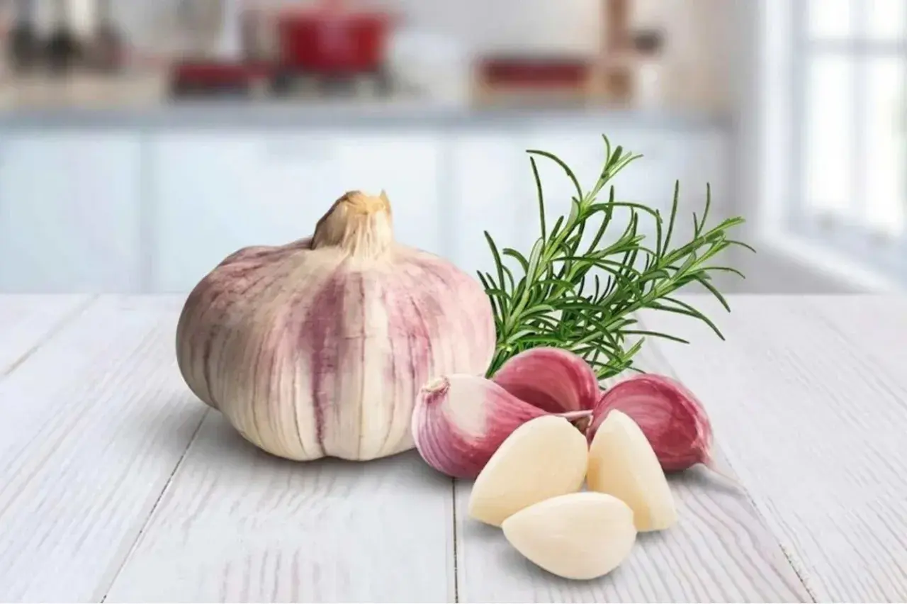 Knoblauchzehen und ein Rosmarinzweig auf einem Holztisch. Vorsicht bei der Zubereitung von Knoblauchöl, um Botulismus zu vermeiden.