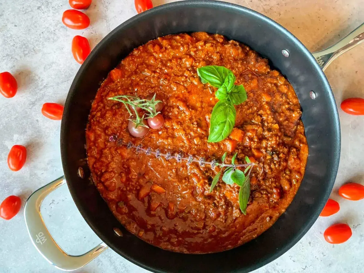 Herzhafte rotwein bolognese in einer Pfanne, garniert mit Basilikum und Kirschtomaten.