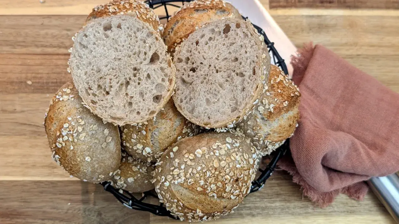 Korb mit knusprigen Haferbrot-Brötchen, eines davon aufgeschnitten, zeigt die luftige Krume.