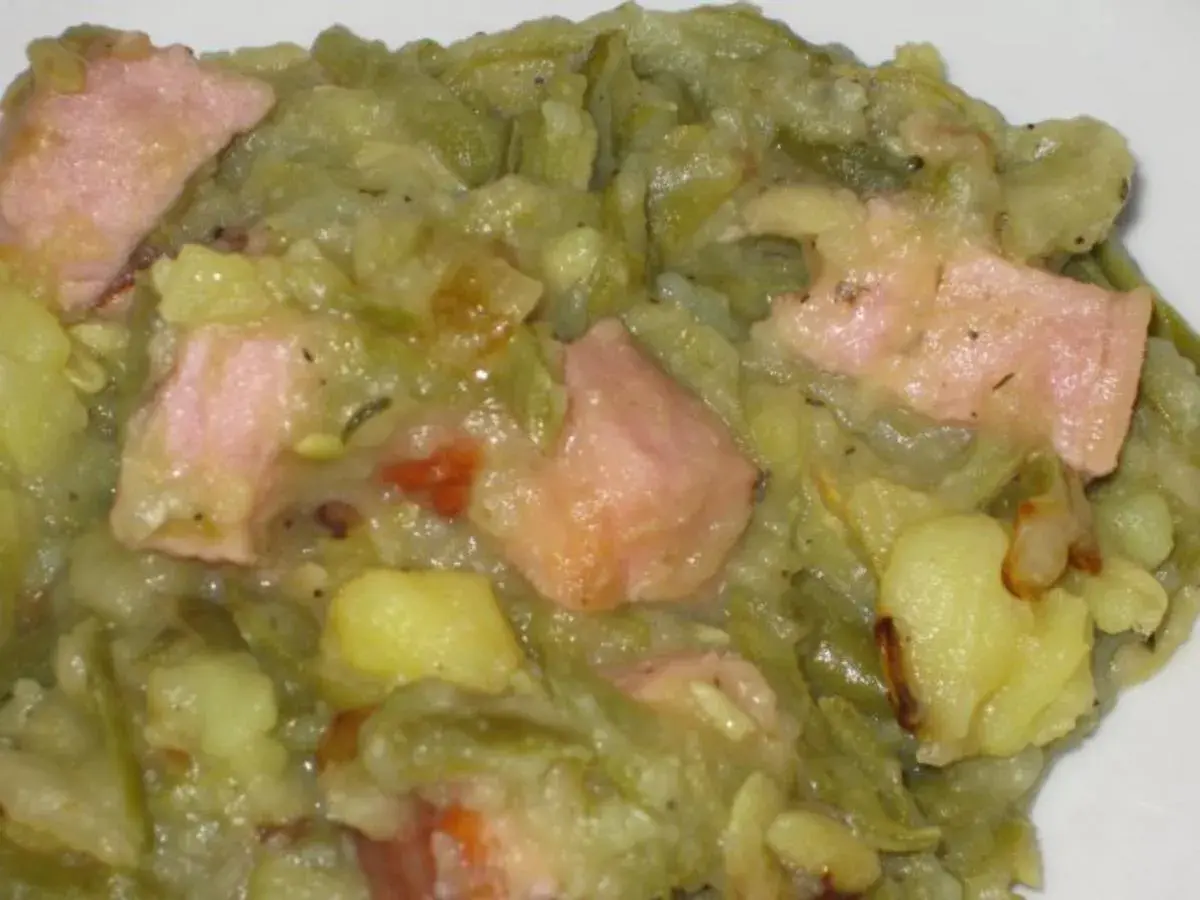 Ein herzhafter saure bohnen eintopf mit Kartoffeln und rosa Speckstücken, dampfend und bereit zum Genießen.