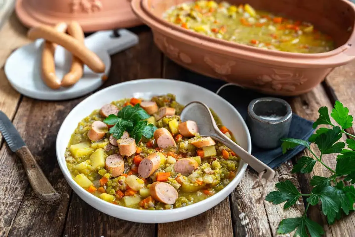 Herzhaftes traditionelles Erbsensuppe Rezept mit Würstchen und Kartoffeln, garniert mit Petersilie.