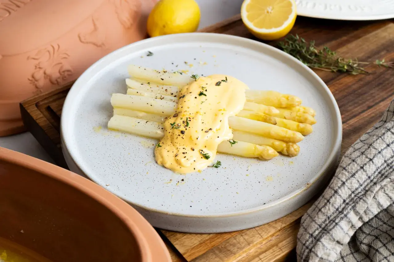 Frischer weißer Spargel aus dem Glas, verfeinert mit cremiger Sauce Hollandaise und Kräutern, garniert mit Pfeffer und Zitronenschale.