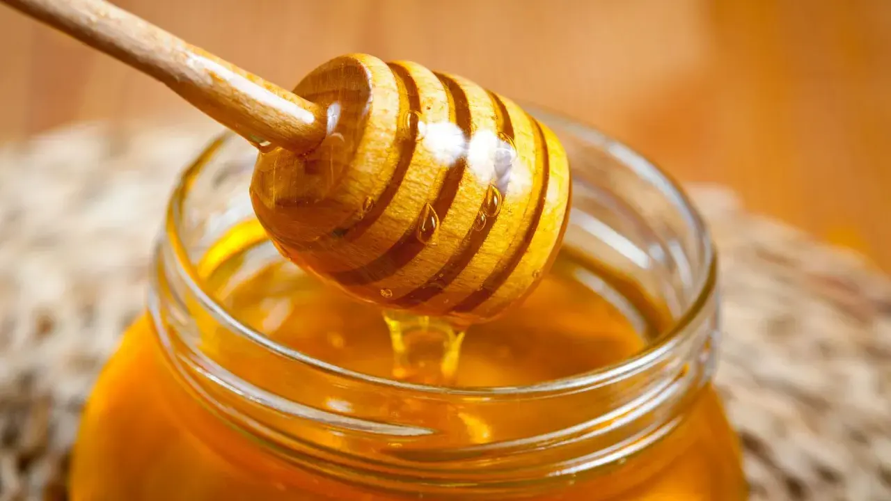 Ein Honigheber aus Holz tropft goldenen Honig in ein Glas. Kein Anzeichen von honig schimmel.