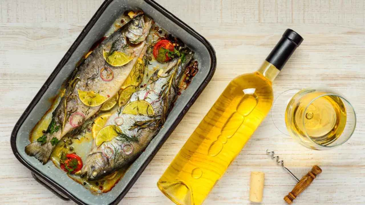 Zwei gebackene Forellen mit Zitrone und Kräutern, daneben eine Flasche Weißwein und ein Glas. Perfekt, welcher Wein zu Lachs passt, ist hier schon fast klar.