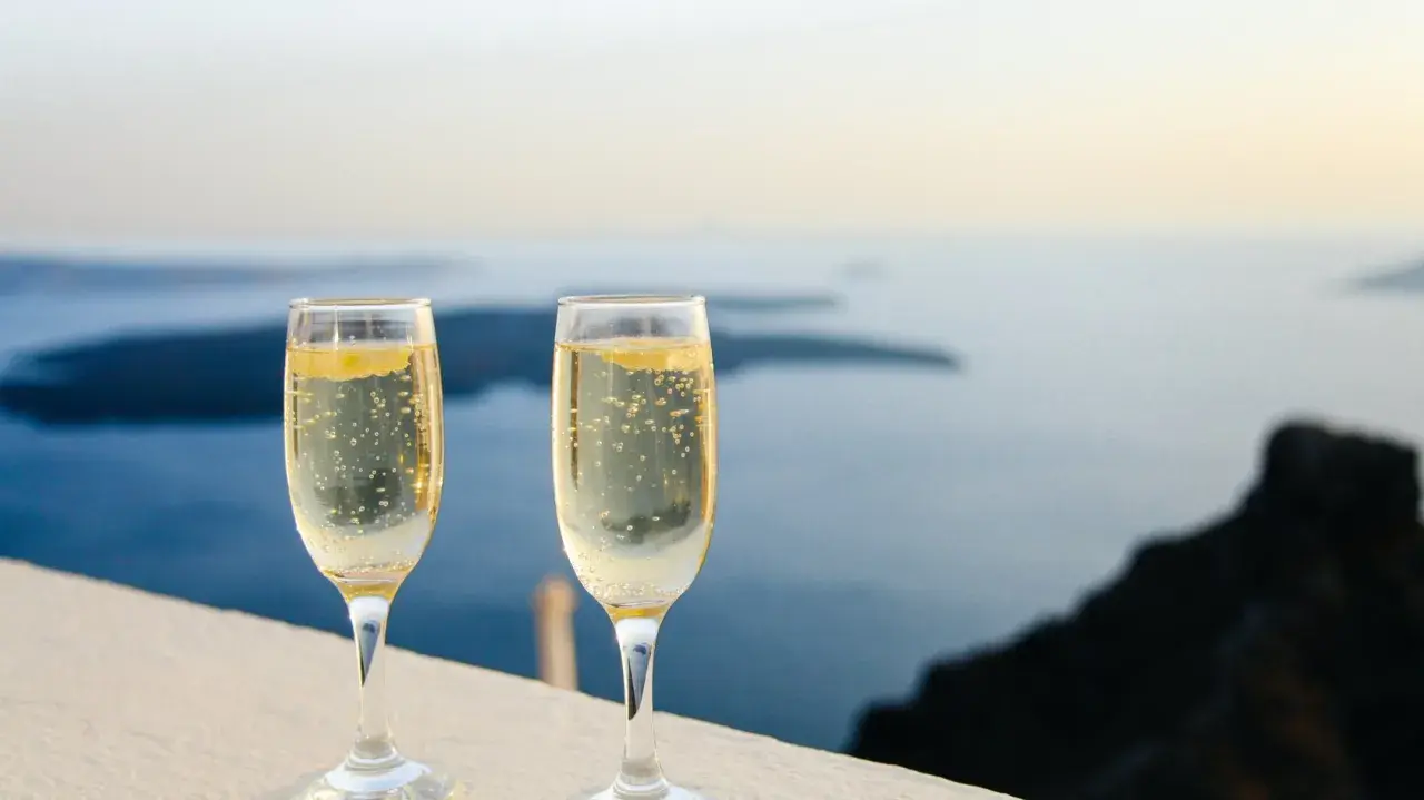 Zwei Gläser Champagner mit Bläschen stehen vor einer Meereslandschaft. Die Frage, wie lange ist Champagner haltbar, beschäftigt Genießer.
